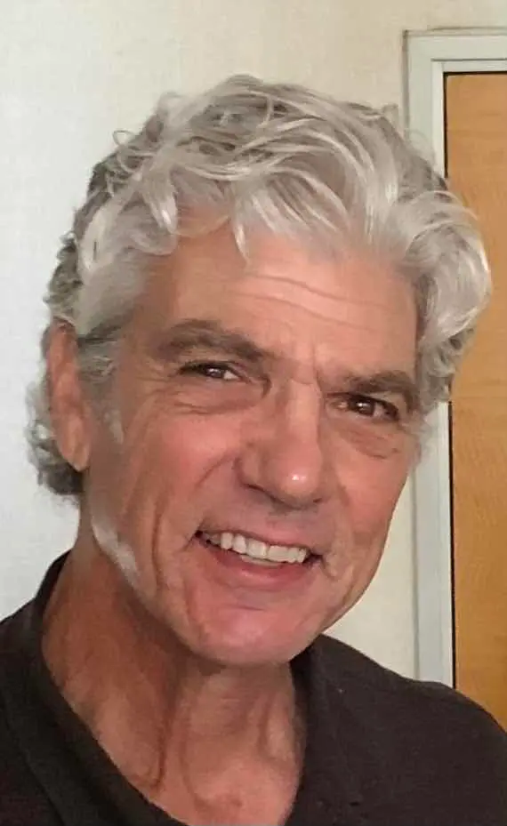 Smiling older man with gray hair and a dark shirt.